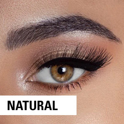 Close-up of a brown eye with long, thick lashes, gold eyeshadow, and bold black eyeliner. The eyebrow is well-groomed, and the word “NATURAL” appears in a white box at the bottom left.