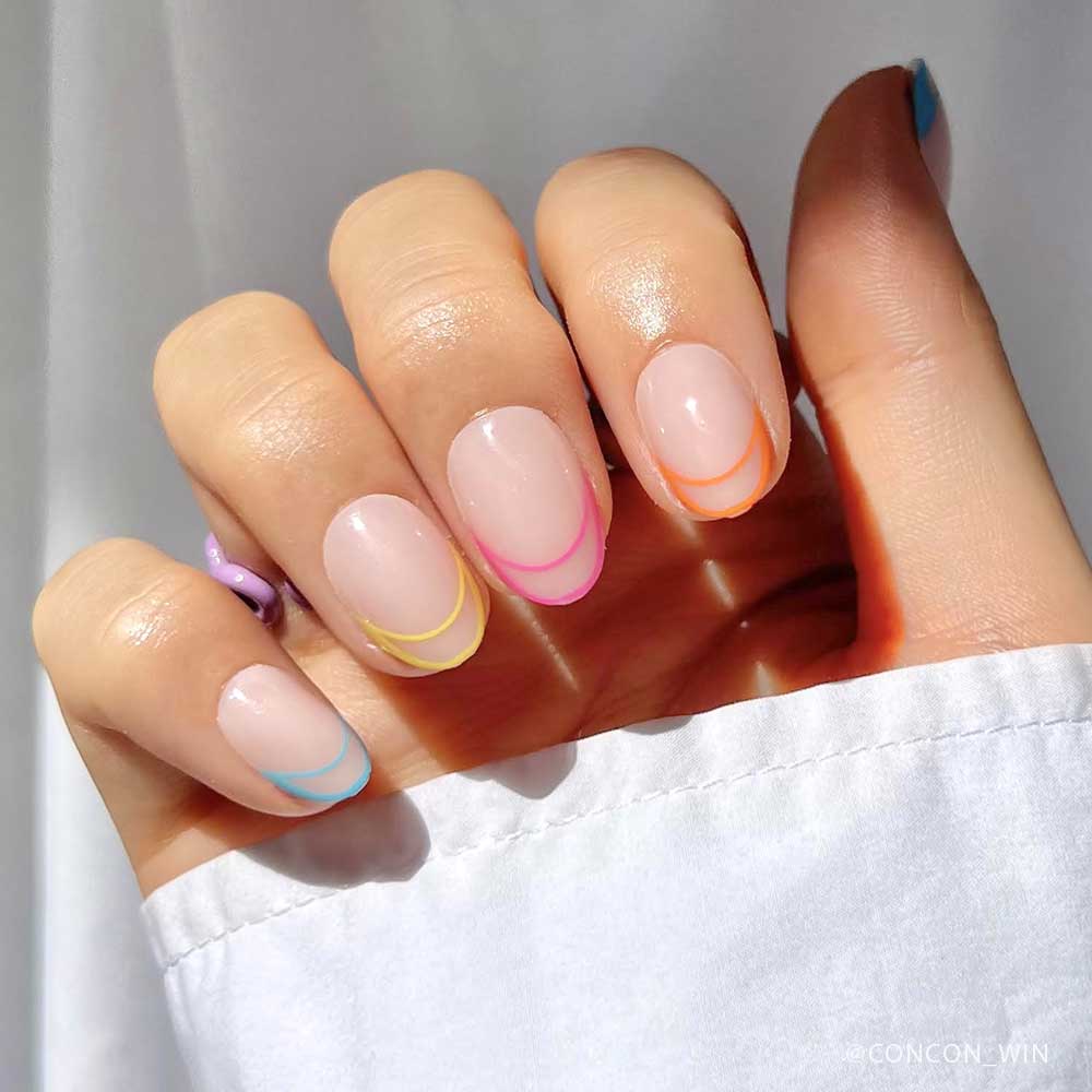 A hand with short oval nails, each featuring sheer nude polish and neon French tips in pink, orange, yellow, or blue—perfect for showing off the glamnetic Neon Lights Nail Set with a white long-sleeve top. - Product image