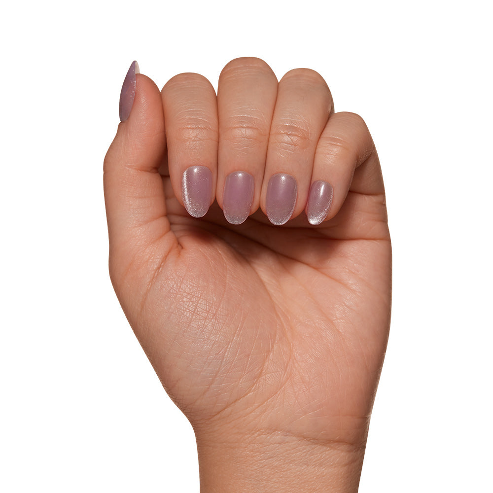 A hand with gently curled fingers displays short oval nails painted in light, shimmery lavender polish from glamnetic’s Fairy Dust set, set against a white background. - Product image