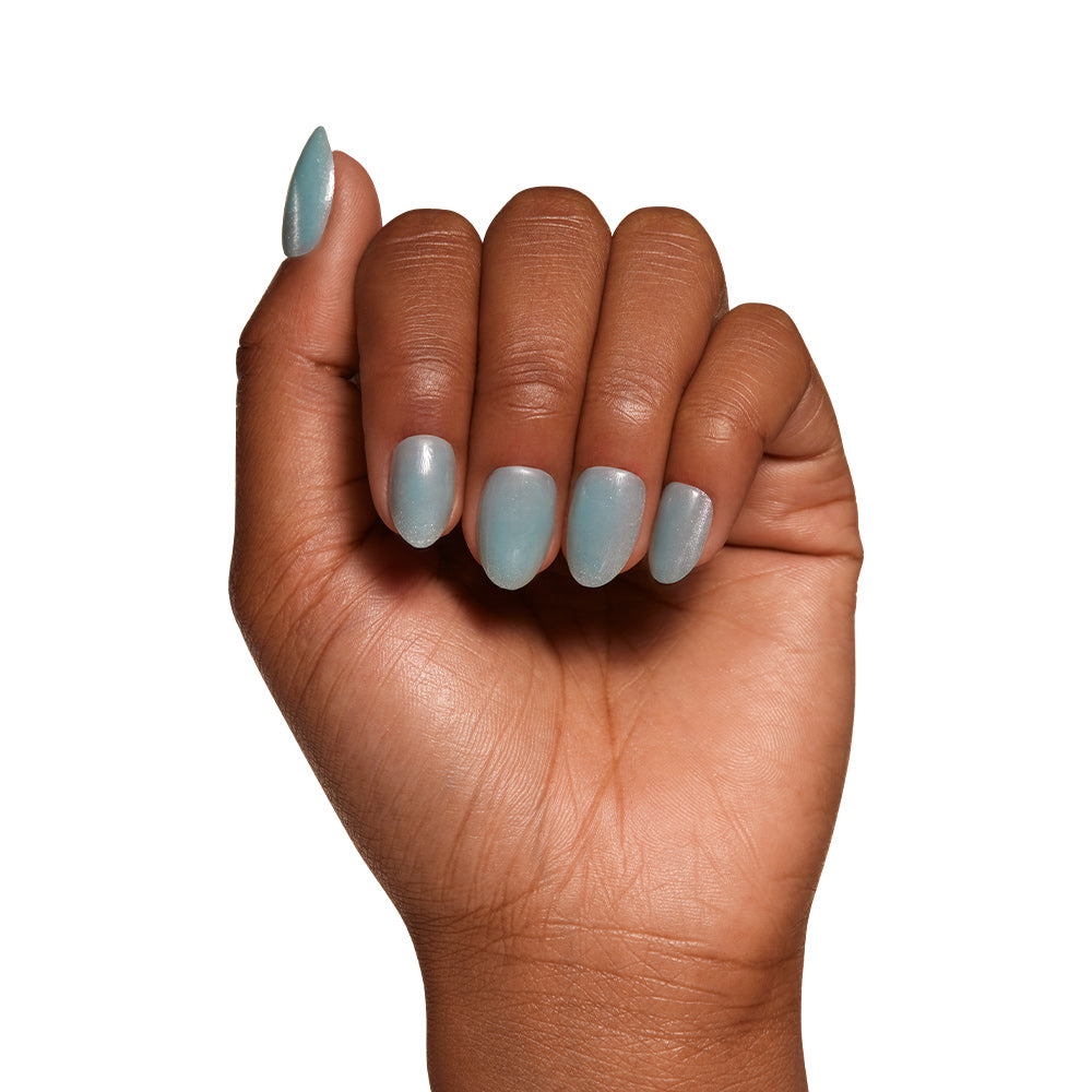 A hand with medium brown skin displays short oval nails in a light blue-gray from the glamnetic Unicorn Tears set, shown in a fist against a white background. - Product image