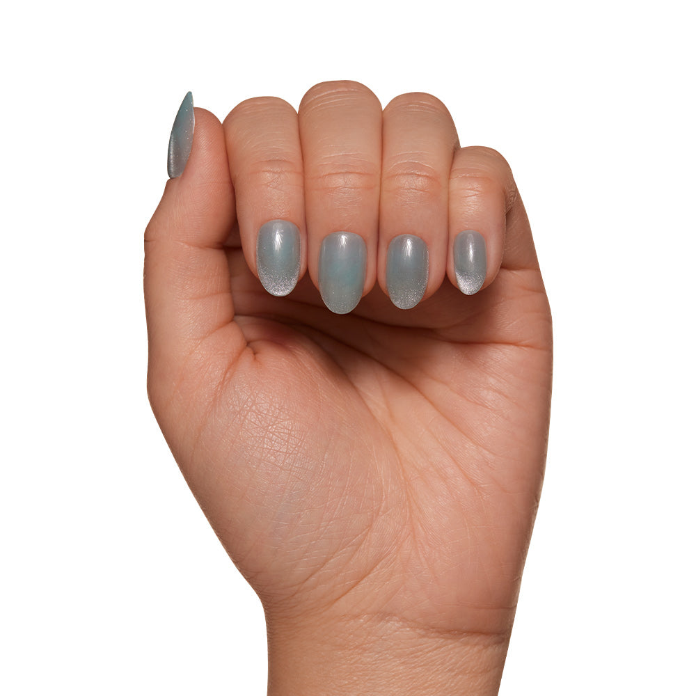 A hand with fingers gently curled shows short oval nails painted in metallic light blue using glamnetic’s Unicorn Tears, set against a plain white background. - Product image