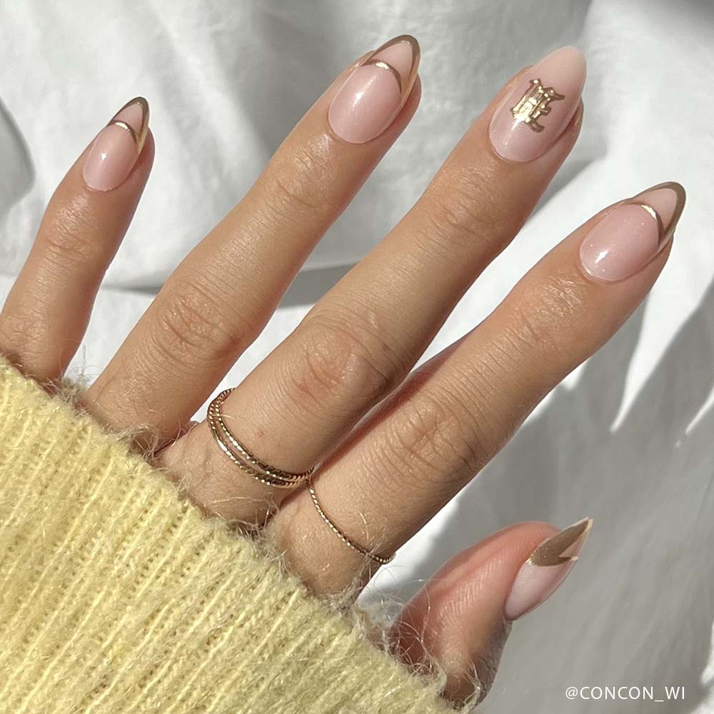 A hand with almond-shaped nails painted in pale pink using glamnetics Hufflepuff™, featuring 3D gold foil tips, a gold accent on the ring finger, and paired with thin gold rings and a yellow knit sweater for a vegan, cruelty-free manicure. - Product image