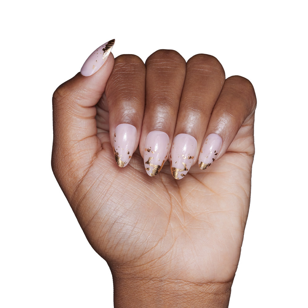 A hand with medium brown skin shows off short, almond-shaped nails in glamnetic’s 24K set—pale pink polish with gold foil-tipped accents—set against a white background. - Product image