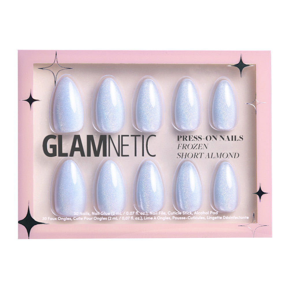 A box of glamnetic Frozen press-on nails features ten short almond-shaped, sparkly iridescent white nails with an icy-blue tint, arranged in two rows against a pink background. - Product image