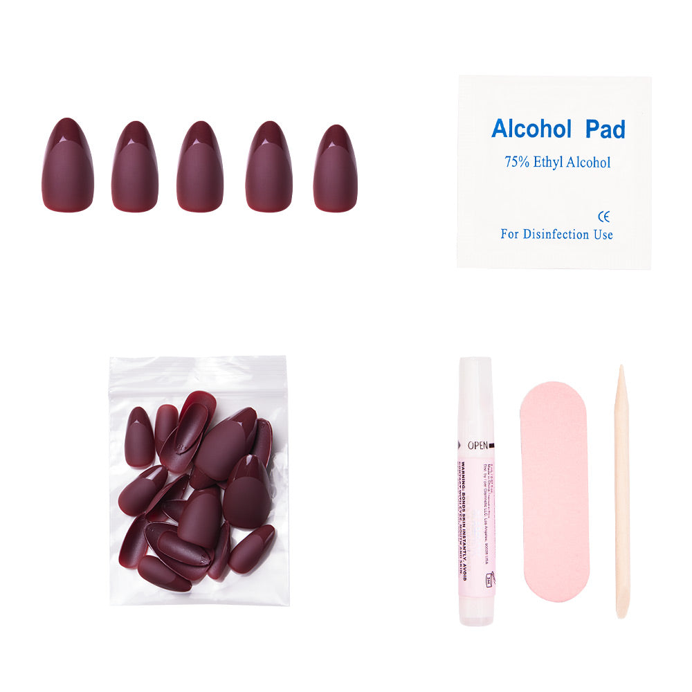 A press-on nail kit with maroon nails, an alcohol pad, a small bag of extra nails, nail glue, a pink nail file, and a wooden cuticle stick laid out on a white background.