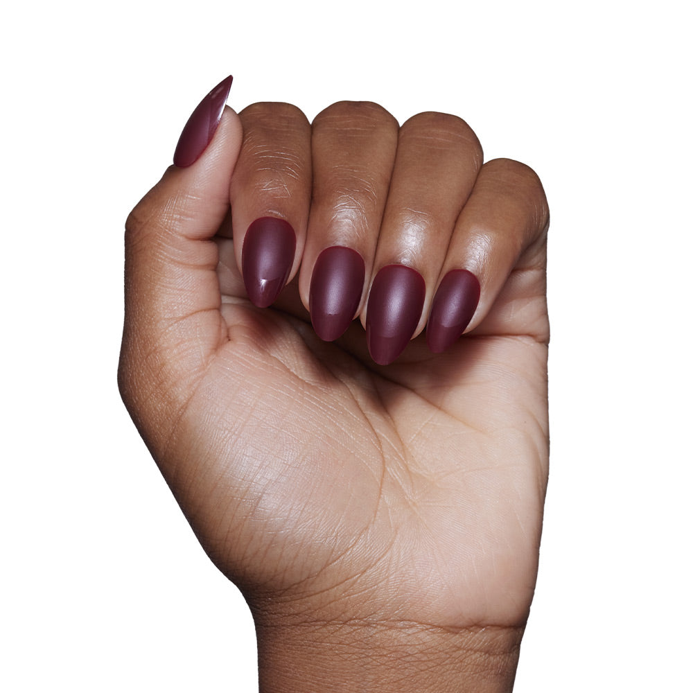 A hand with medium brown skin displays long, almond-shaped nails in the glamnetic Merlot matte set. The fingers are slightly curled against a plain white background. - Product image