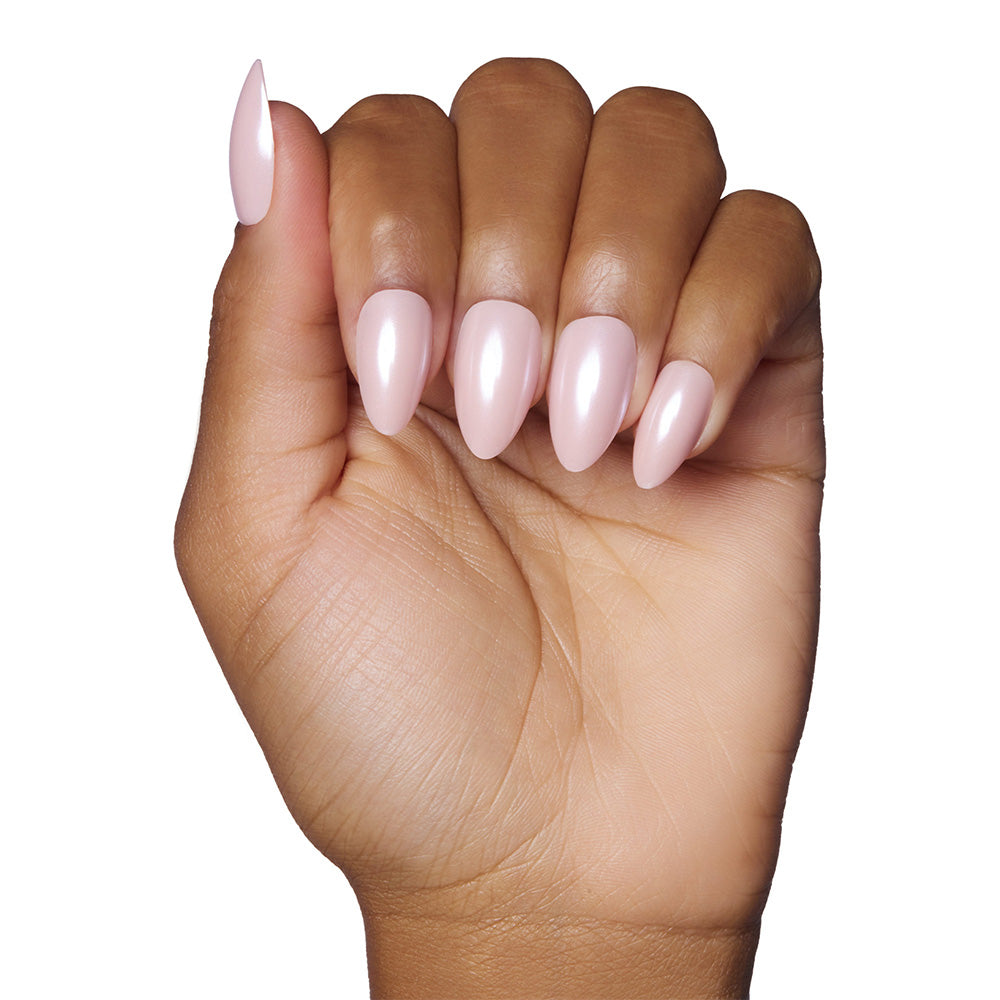 A hand with medium-brown skin shows short almond-shaped nails painted in a glossy blush pink using glamnetic’s First Kiss, set against a white background. - Product image