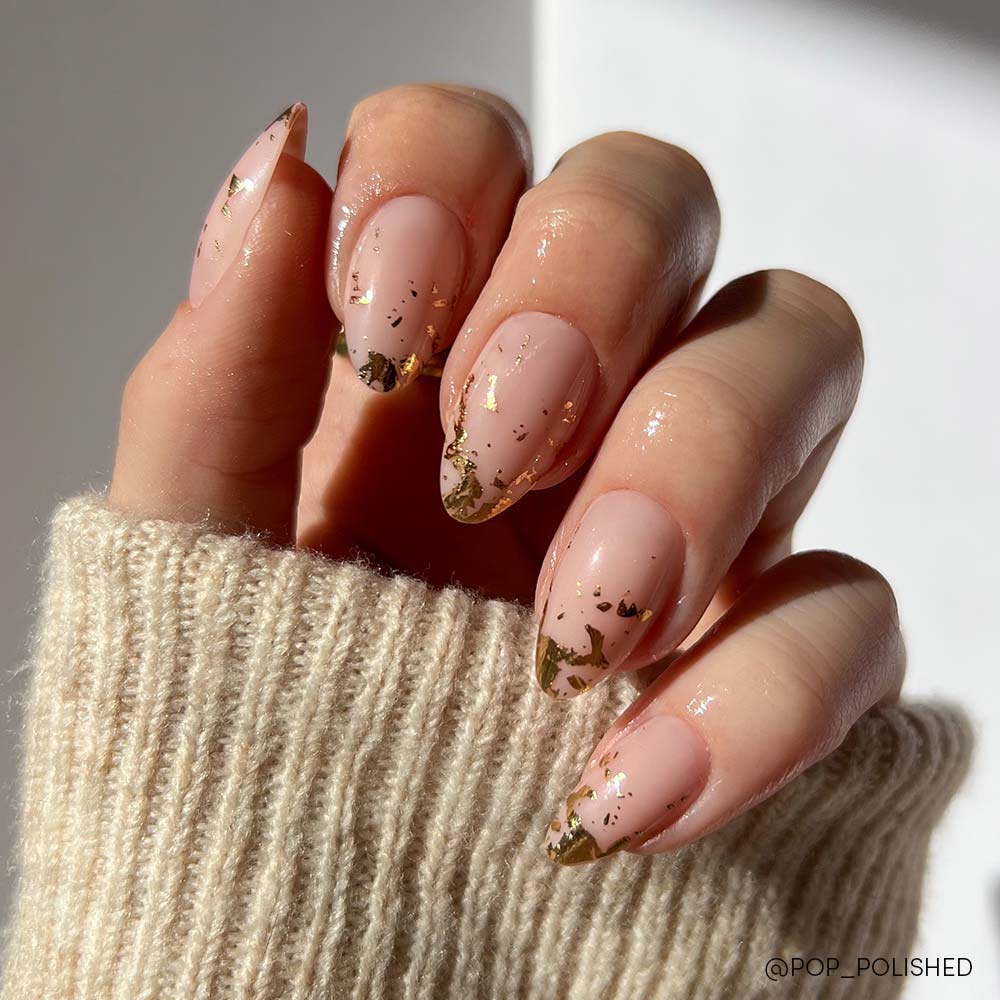 The glamnetic 24K short almond press-on nails showcase a nude pink base with gold foil details, complemented by a cream knitted sweater sleeve. - Product image