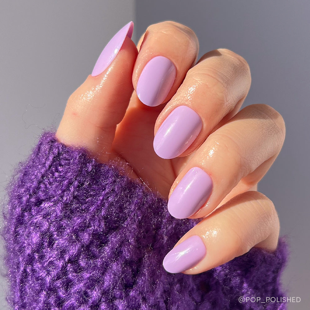A hand with neatly manicured, oval-shaped nails painted in glamnetic’s Lilac set wears a textured purple knit sweater, shown against a softly lit background. - Product image