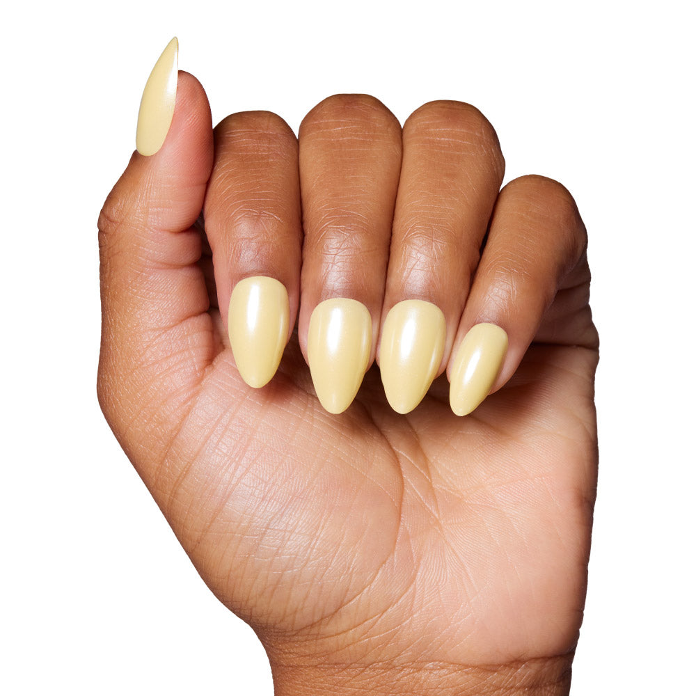 A hand with medium brown skin shows long, almond-shaped press-on nails in glossy pastel yellow from the glamnetic Yellow Pop set, displayed against a white background. - Product image