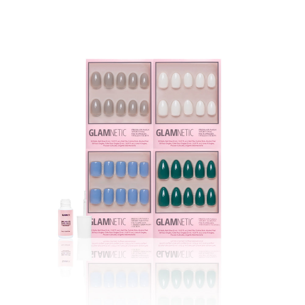 Four Glamnetic Frosted Fantasy press-on nail sets—Gray, White, Blue, and Jewel-Toned Green—are shown in pink packaging. An opened white bottle of vegan, cruelty-free nail glue sits beside them on a white background. - Product image