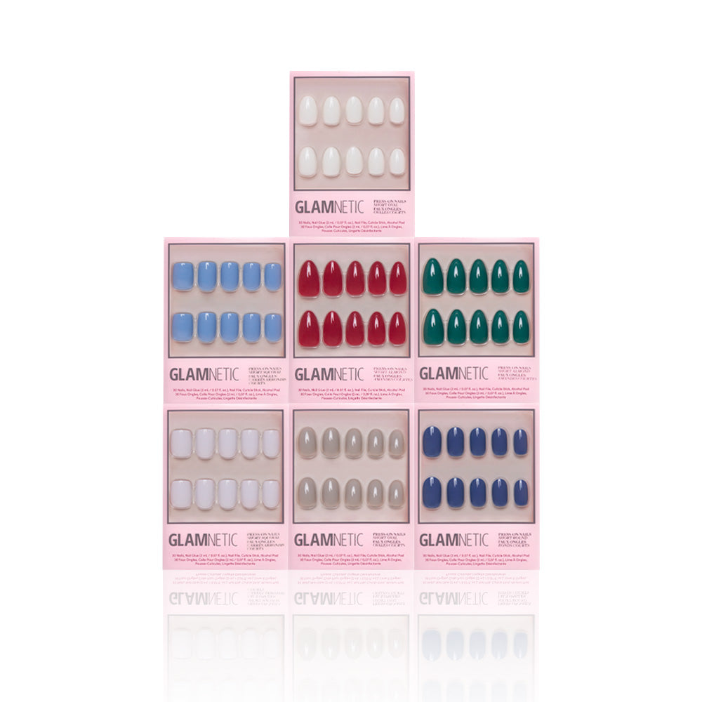 Seven boxes of glamnetic Winter Opulence press-on nails, in white, blue, red, green, and beige shades, are arranged pyramid-style on a white background. The collection adds elegance for perfect at-home manicures. - Product image