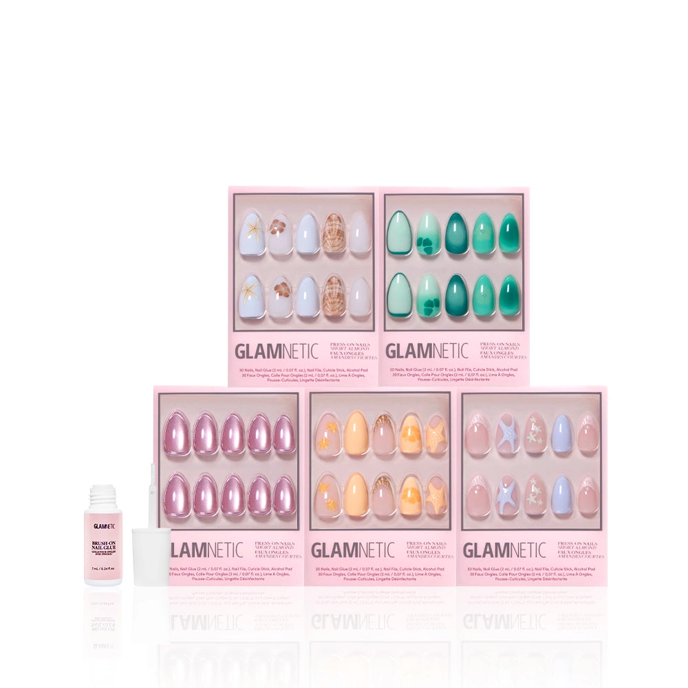 Five boxes of glamnetic Ann’s Cove press-on nails with assorted colors and designs—featuring coastal scenes and 3D art—are arranged in two rows beside a small nail glue bottle, all set against a white background. - Product image