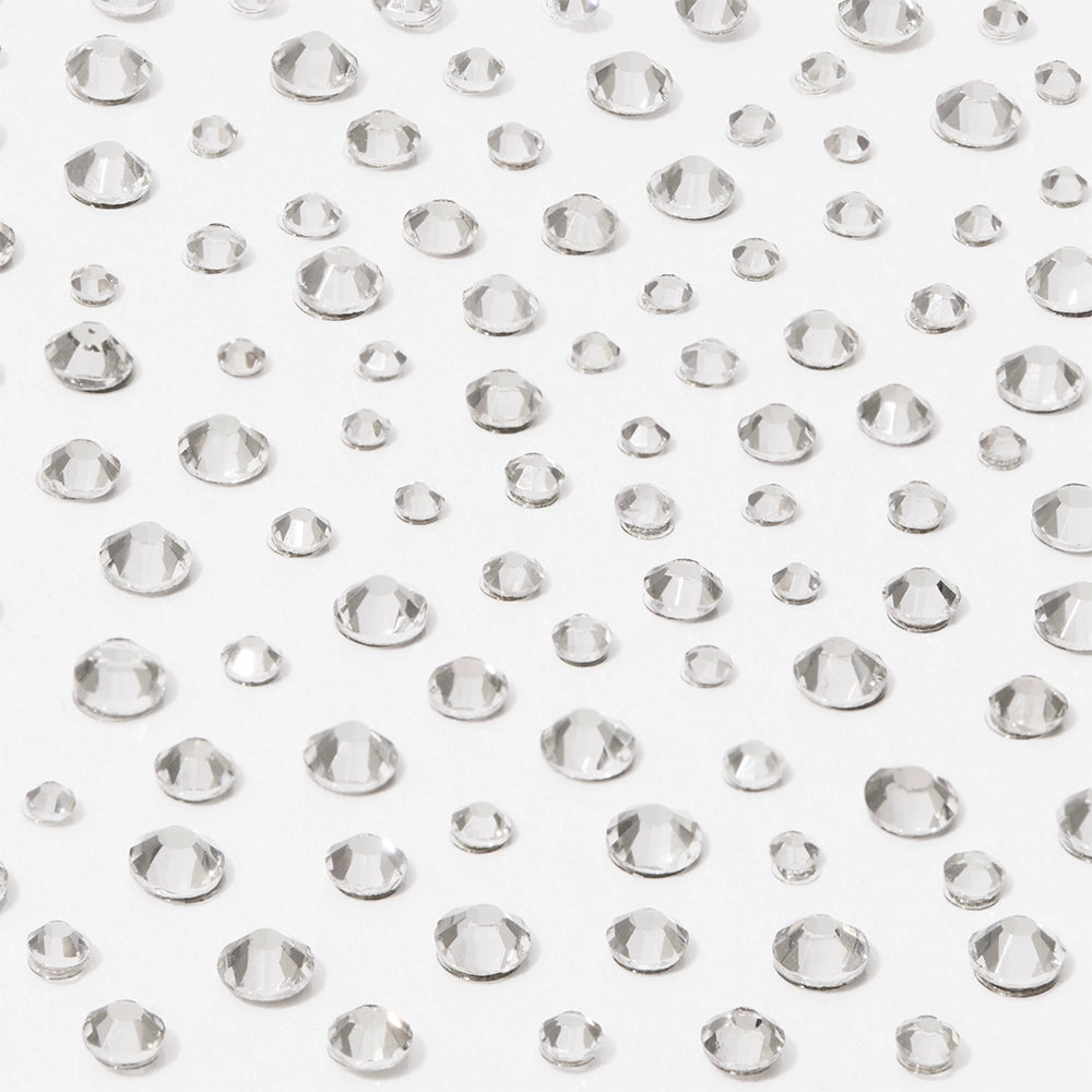 Multiple clear, round, faceted gems of different sizes are scattered on a white surface, creating a sparkling effect—perfect to use with glamnetic’s A Gem Nail Decal Stickers for stunning nail art designs.