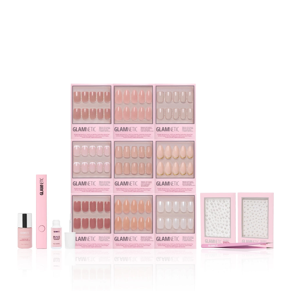 The glamnetic Timeless Studio Kit features a variety of pink and nude press-on nails with glue, file, cuticle stick, remover, and two Nail Decal Sticker sheets, all neatly arranged in pink packaging against a white background. - Product image