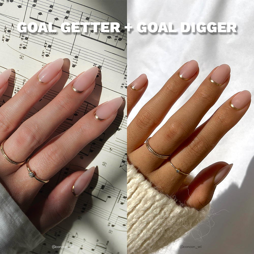 Two hands wear glamnetics Goal Getter + Goal Digger nude almond nails with gold reverse French tips. The left hand rests on sheet music, the right on a plain background—both accessorized and styled with a cozy cream sweater. - Product image