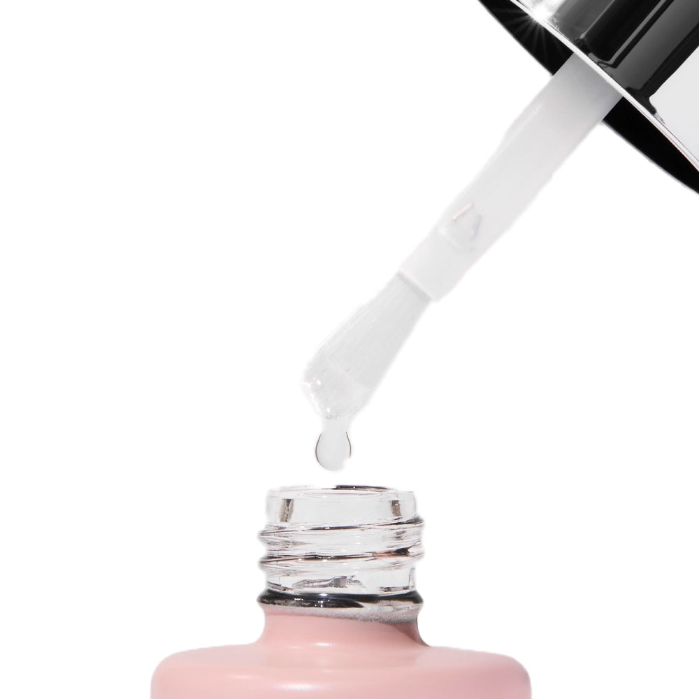 A close-up of a nail polish brush with a clear drop about to fall into an open light pink bottle, ideal for a salon-quality look when you pair it with the glamnetic UV Gel Clear Top Coat. - Product image