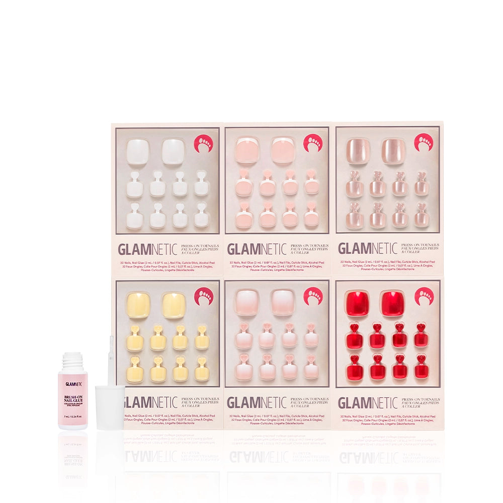 Glamnetic Glazed & Glossy Pedi Bundle displayed alongside a pink bottle of brush-on nail glue. Includes six unique press-on toenail kits arranged neatly in soft-toned packaging featuring glossy finishes and shimmer details. - Product image