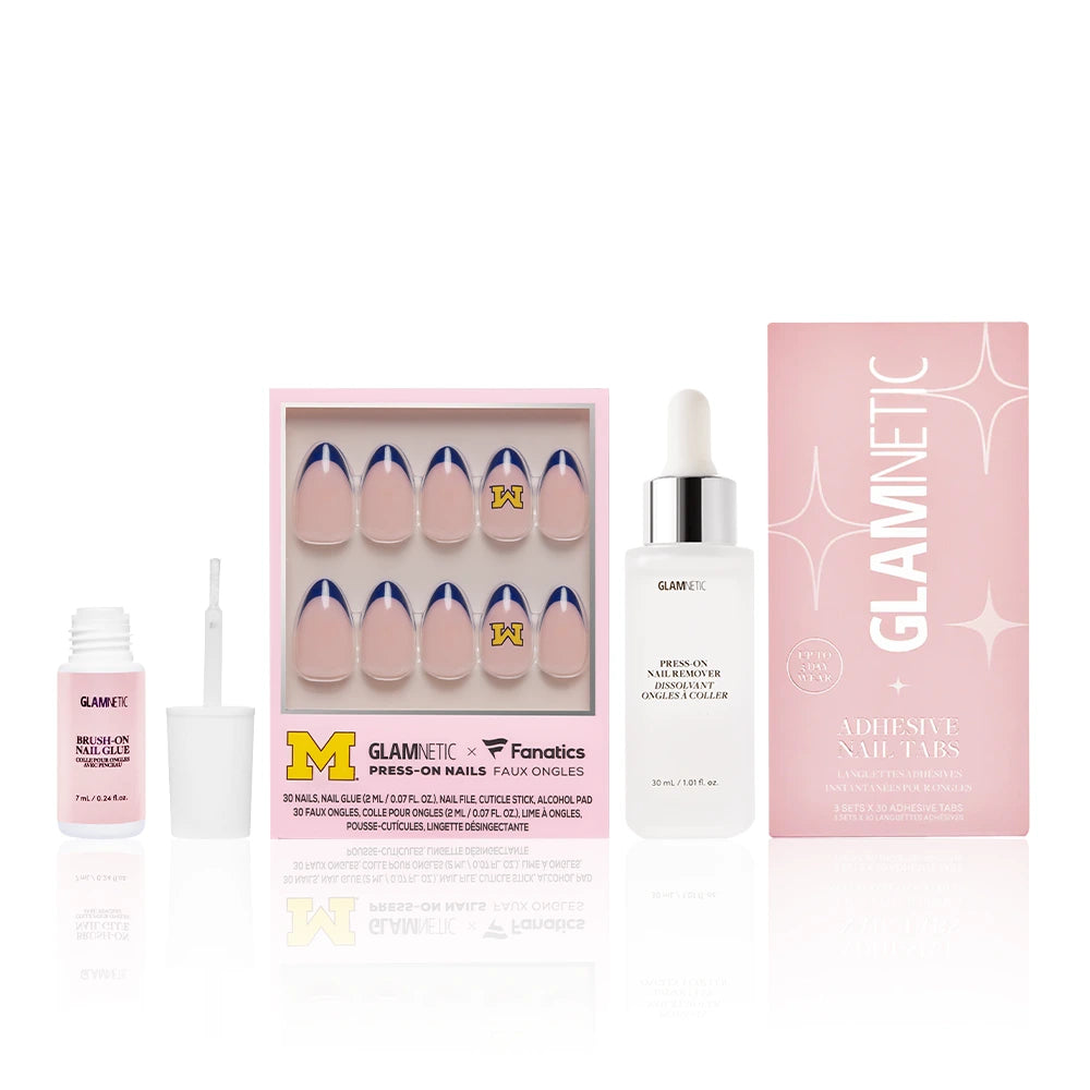 The glamnetic The Michigan Wolverines Gameplan set includes press-on nails with Wolverine-blue French tips and University of Michigan logos, nail glue, adhesive tabs, and Press-on nail remover, all beside a pink glamnetic box. - Product image