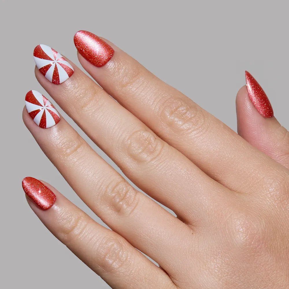The glamnetic Candy Crush holiday nail set features shiny red nails with two accent nails sporting a festive peppermint swirl, all standing out against a plain gray background. - Product image
