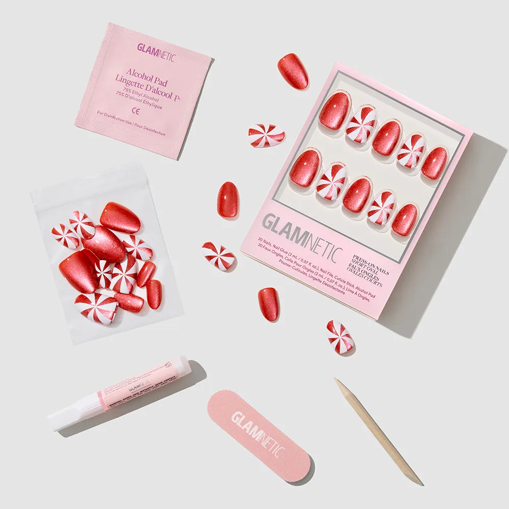 The Candy Crush press-on nails set by glamnetic features red and peppermint swirl nails, nail glue, alcohol pad, nail file, cuticle stick, and extra nails arranged neatly on a light gray background. - Product image