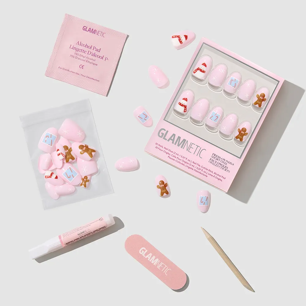 The glamnetic Cocoa & Kisses set features short oval nails with gingerbread and holiday designs, plus a nail file, cuticle stick, nail glue, alcohol pad, and extra nails, all displayed on a light gray surface. - Product image