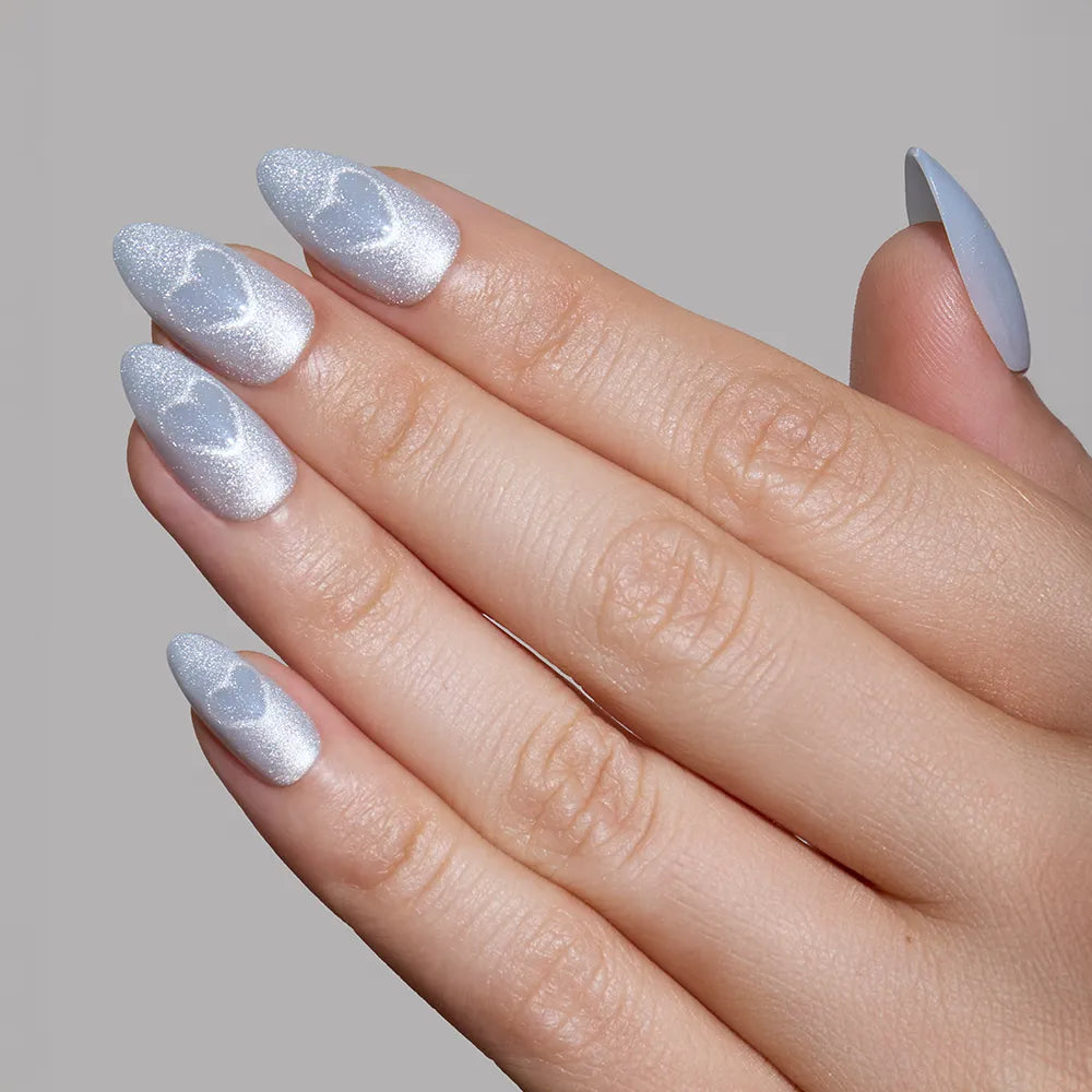A hand with long, almond-shaped nails painted in shimmery silver, featuring glossy, translucent swirls inspired by glamnetic's Cold Hearted Nail Set, displayed against a plain gray background. - Product image