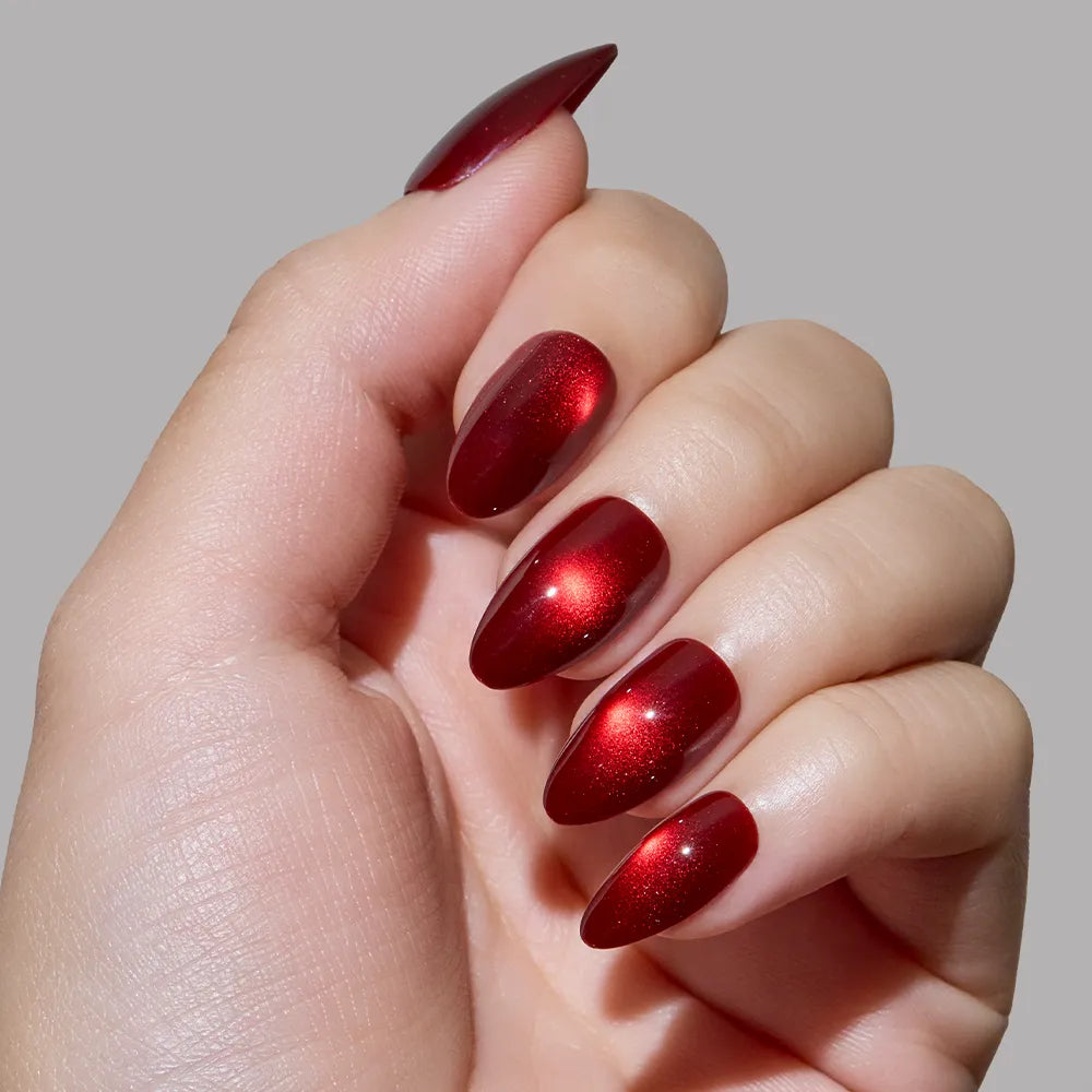 A hand with short almond nails, painted in the shiny, metallic red Frosted Cranberry polish by glamnetic, is displayed against a plain gray background. - Product image