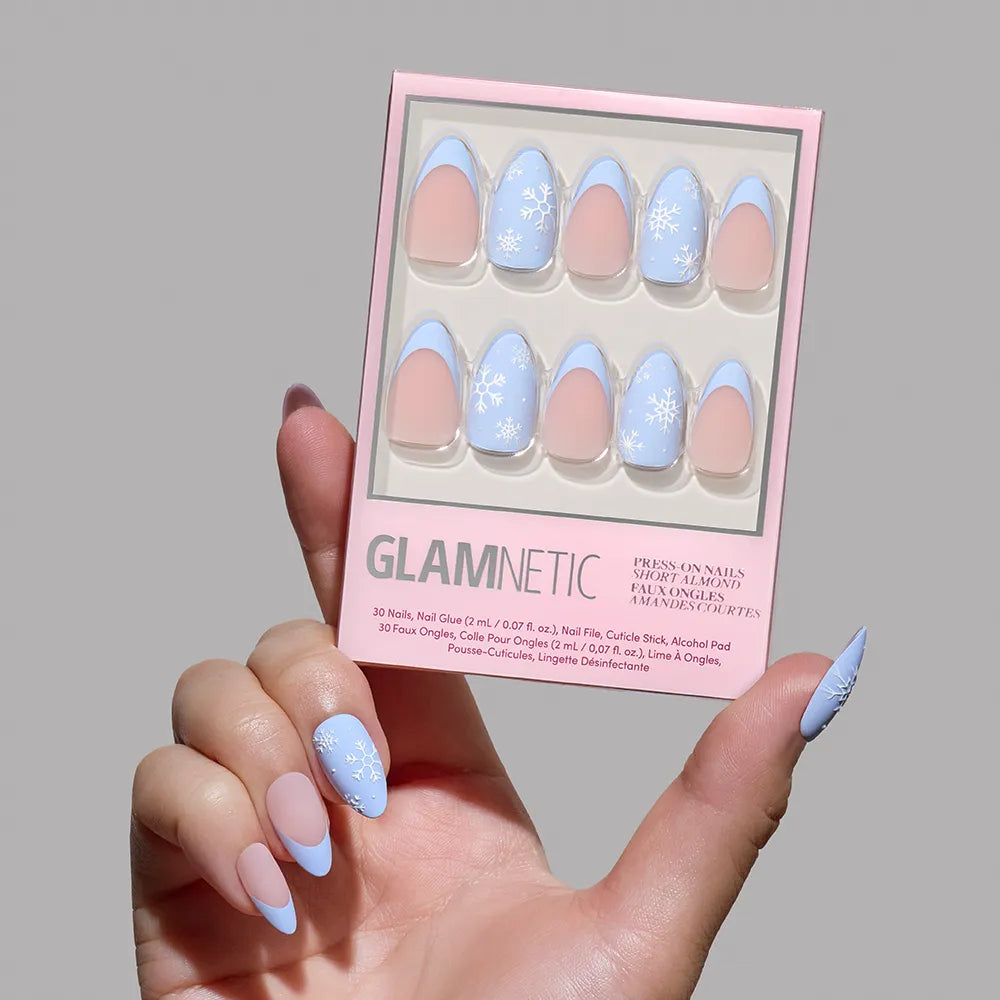 A hand with long, matte almond nails in pink with blue tips holds a box of glamnetic Snow Bunny Nails, a winter set featuring pastel blue, pink, and white snowflakes. - Product image