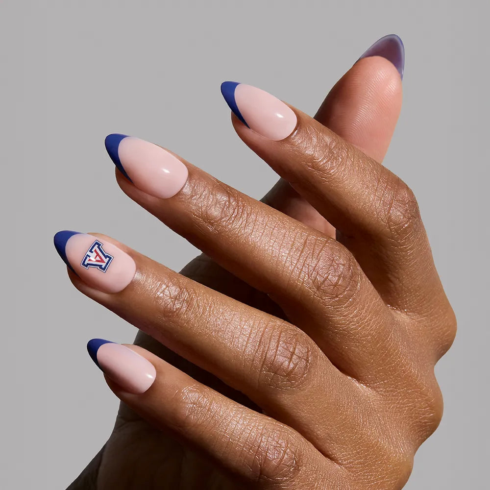 A hand showcases almond-shaped, salon-quality nails with a nude base and navy French tips from the glamnetic Arizona Wildcats Press-On Nail Set; the thumb features a red, blue, and white Wildcats V logo against a light gray background. - Product image