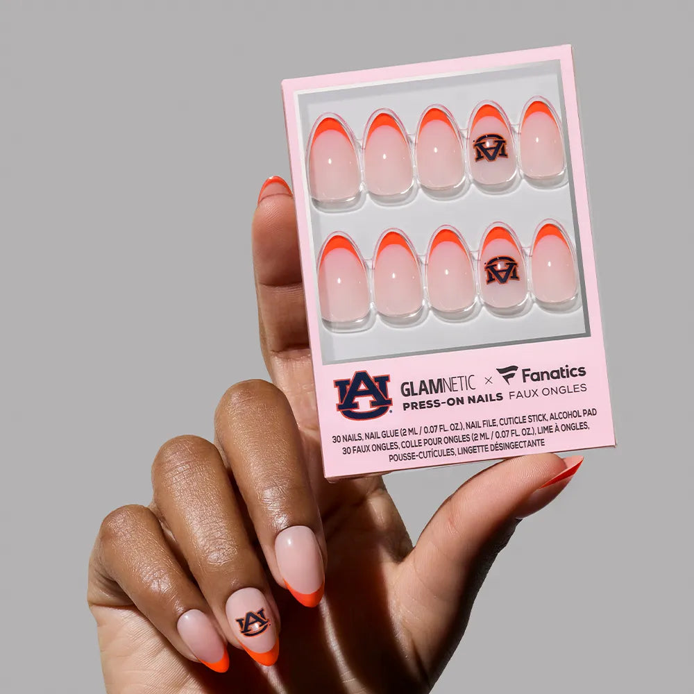 A hand holds a glamnetic Auburn Tigers Press-On Nail Set box, with orange tips and team logo nail art. One nail with the Auburn logo is worn on their finger. - Product image