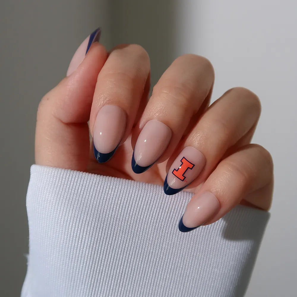 The glamnetic Illinois Fighting Illini Press-On Nail Set features blue French tips with a nude base and an orange "I" on the ring finger, perfect for fans. A white sleeve partially covers the hand, adding a stylish finishing touch. - Product image