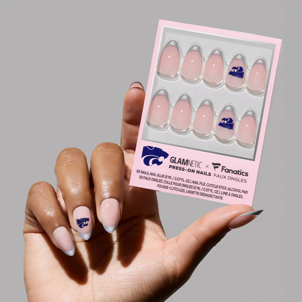 A hand with pink press-on nails, featuring Kansas State Wildcats nail art on the ring finger, holds a glamnetic Kansas State Wildcats Press-On Nail Set with the wildcat logo on one of the nails in the package. - Product image
