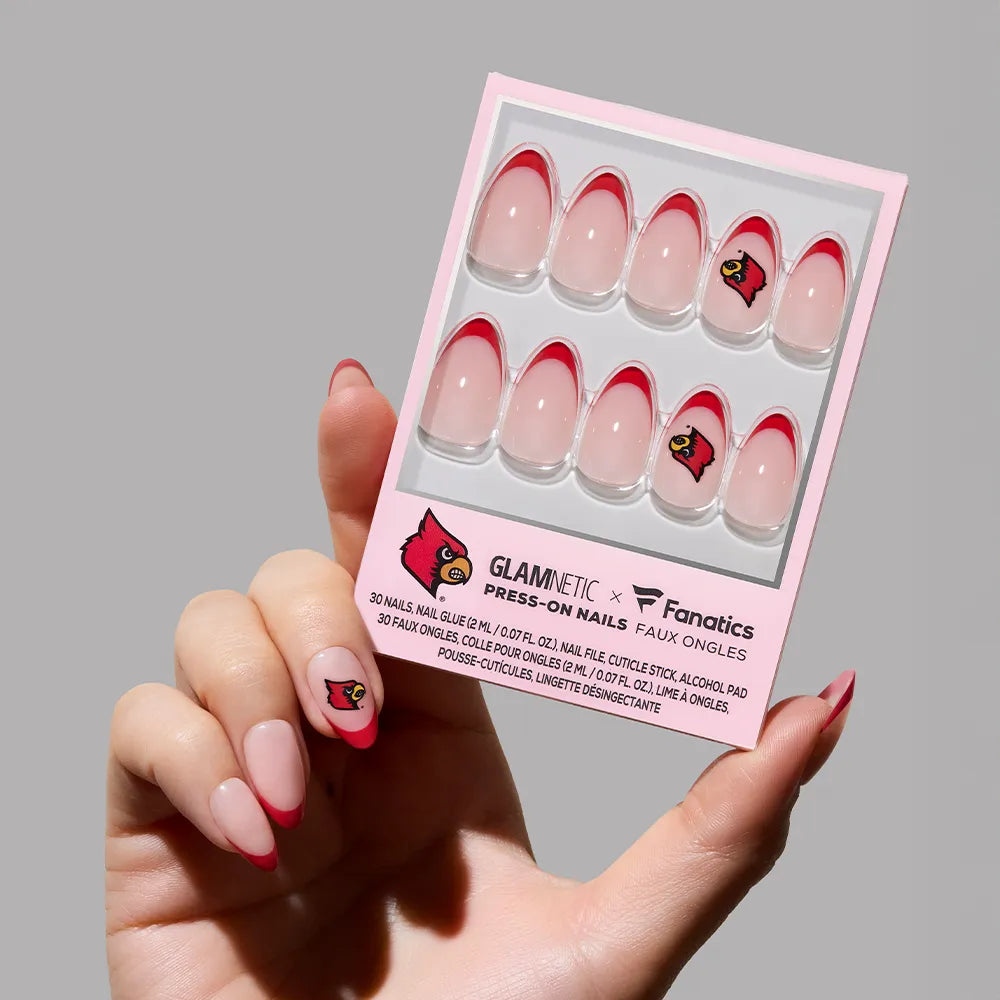 A hand displays the glamnetic University of Louisville Cardinals Press-On Nail Set, featuring a pink base, red French tips, and logo accents. The wearer’s nails match this officially licensed fan manicure in the package. - Product image