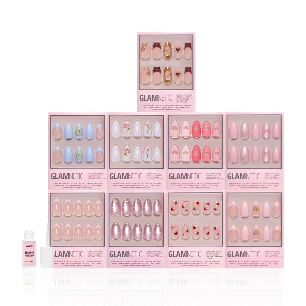 Ten boxes of glamnetic Love in 3D press-on nails are stacked pyramid-style, displaying pastel pink designs with almond shapes and 3D pearl accents. A small bottle of nail glue is placed at the front left. - Product image