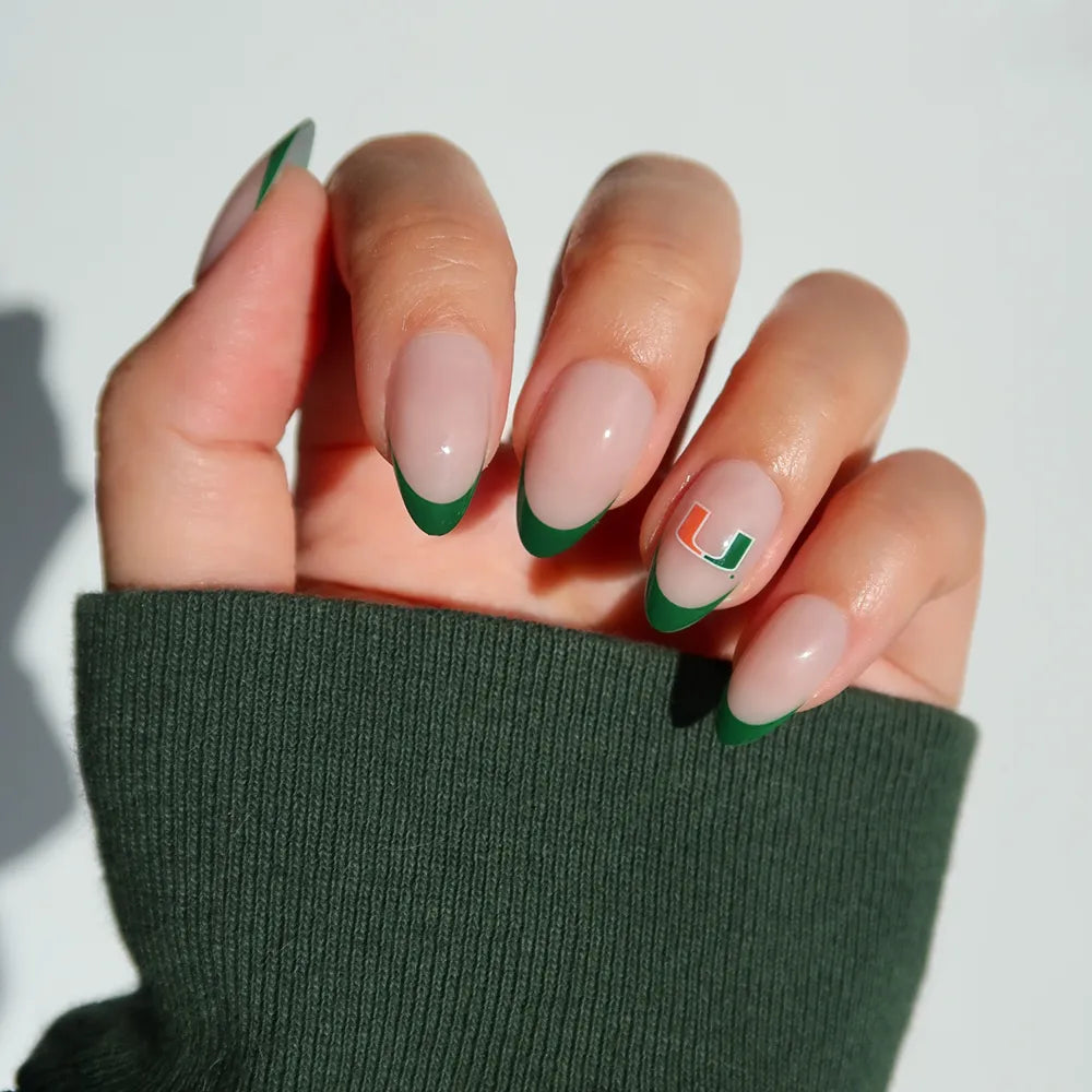 Show off your Miami pride with the glamnetic Miami Hurricanes Press-On Nail Set—almond-shaped green French tips and a standout green and orange U logo accent, paired here with a dark green long-sleeve shirt. - Product image
