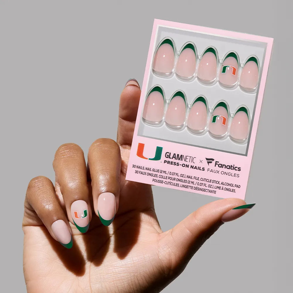 A hand with glamnetic Miami Hurricanes Press-On Nail Set, featuring a green French tip and the U logo, holds a GLAMNETIC x Fanatics package, highlighting salon-quality team logo nails. - Product image