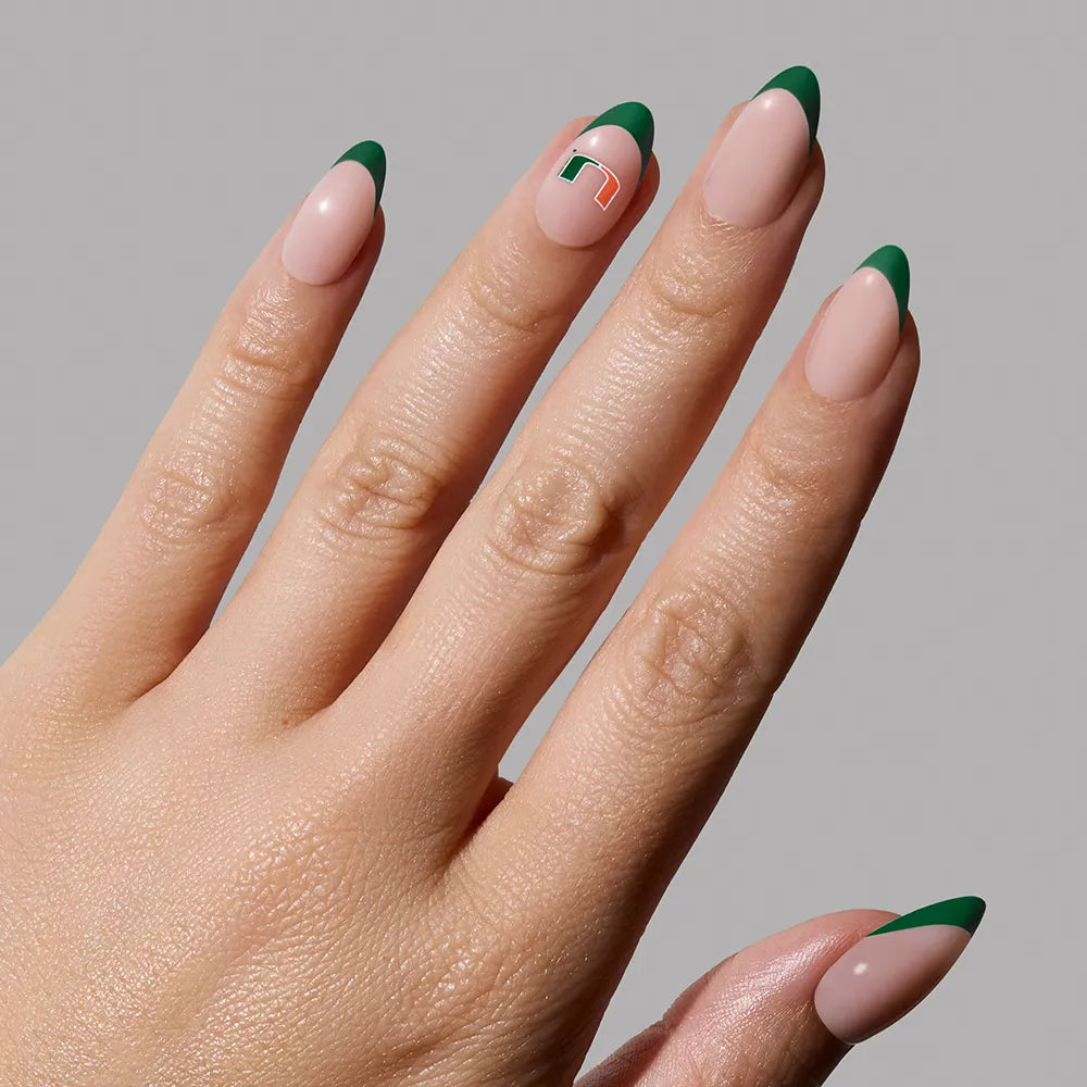 A hand with manicured green French tip nails from glamnetic’s Miami Hurricanes Press-On Nail Set features a ring fingernail with a green and white geometric accent—perfect for fans of trending, sporty styles. - Product image