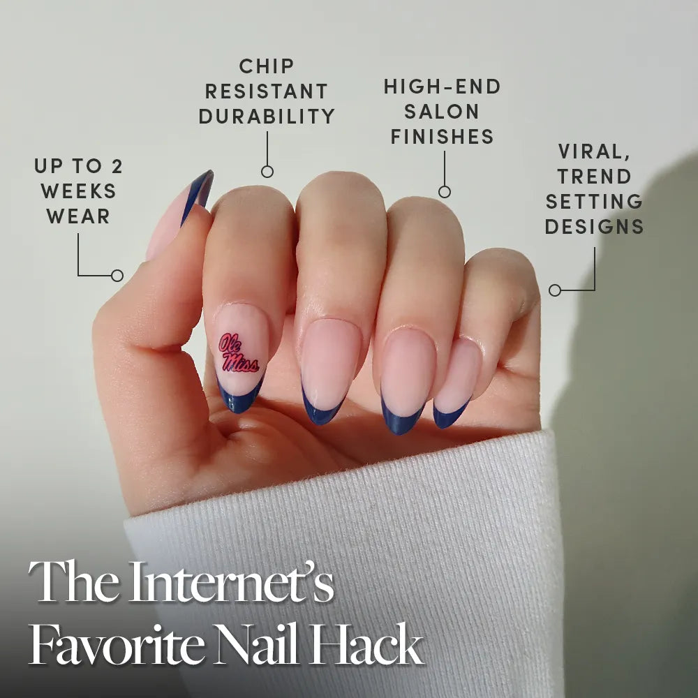 A hand with long, almond-shaped nails featuring a nude base and dark blue French tips. The glamnetic Mississippi Rebels Press-On Nail Set offers up to 2 weeks of chip-resistant, salon-quality wear in trendsetting designs—The Internet’s Favorite Nail Hack. - Product image