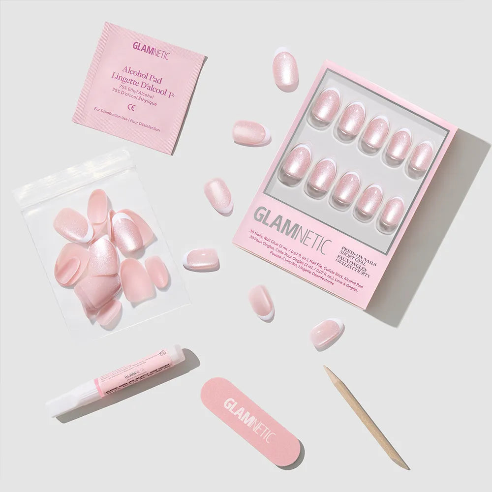 A set of Angelic Touch pink press-on nails by glamnetic in a short oval style, with nail file, cuticle stick, adhesive tube, alcohol pad, and extra nails arranged neatly on a white surface. All accessories feature the glamnetic brand. - Product image
