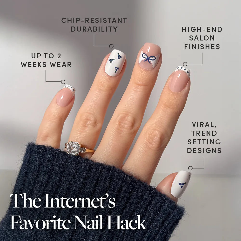 A manicured hand with Blue A Kiss squoval press-on nails by glamnetic, featuring minimal dots, a bow, lace, and blueberry accents. Chip-resistant, long wear, salon-quality and trendy. Text: The Internet’s Favorite Press On Nail Hack. - Product image