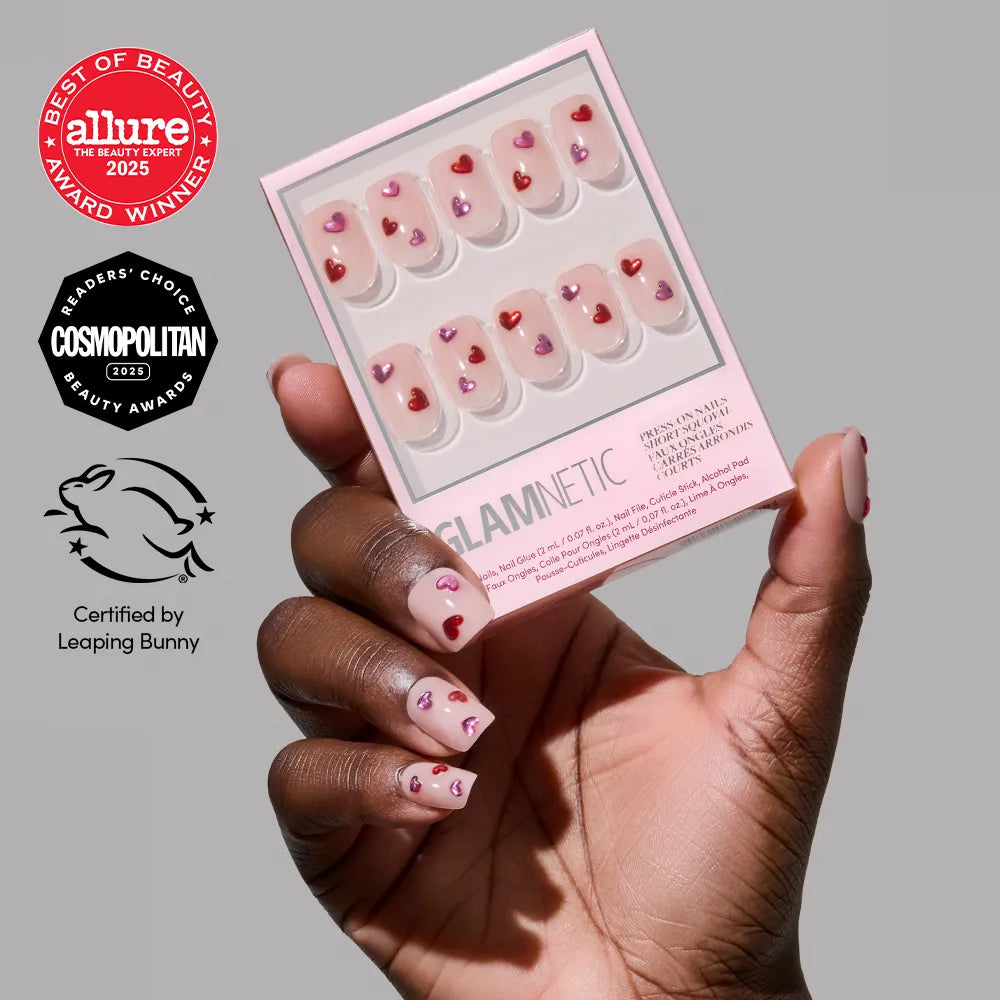 A hand holds a glamnetic Dear Lover press-on nails box with heart and 3D gemstone designs. The matching short squoval nails are worn. Allure, Cosmopolitan, and Leaping Bunny award logos appear nearby.