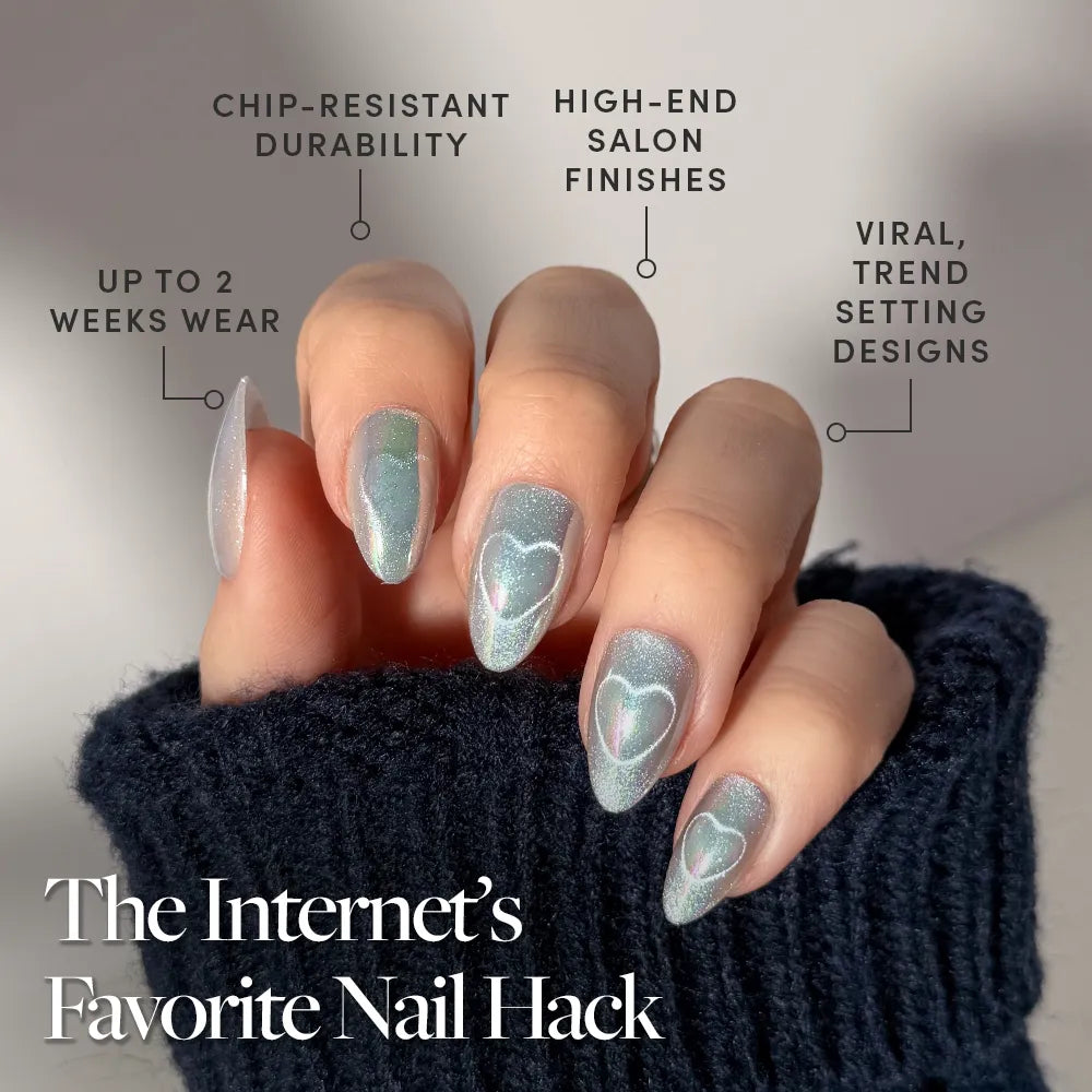 A hand with long, almond-shaped nails painted in glamnetic's Electric Lover—shimmery blue polish with white hearts for a fairy-core look. Features chip-resistant durability, high-end finish, viral design, up to 2-week wear. Sweater sleeves peek out. - Product image