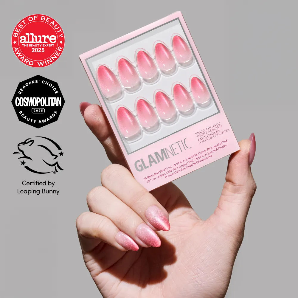 A hand holds a pink box of glamnetic Faded Feelings almond press-on nails in an ombré pink design. Allure, Cosmopolitan, and Leaping Bunny award logos appear on the left. Achieve chic ombré or trendy pink velvet nails with this set.