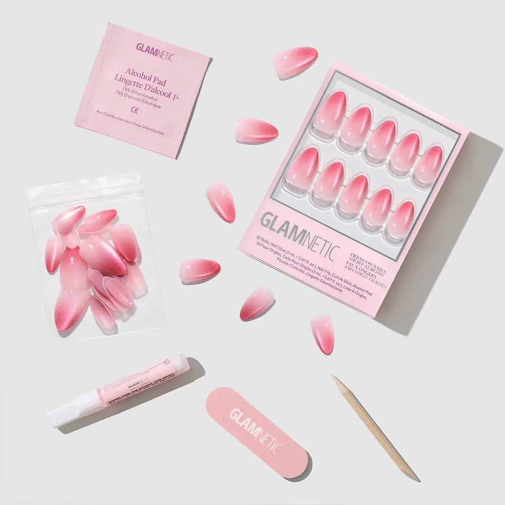 The glamnetic Faded Feelings set includes pink velvet ombré almond press-on nails, a nail file, wooden cuticle stick, alcohol pad, glue tube, and extra nails arranged neatly on a light gray background. - Product image
