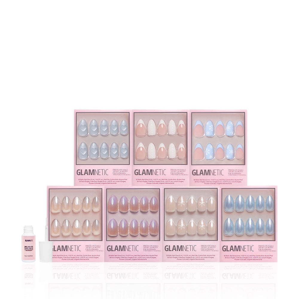 Eight boxes of glamnetic Frozen Over press-on nails in pastel shades, including a short almond winter design set, are arranged in two rows with a small nail glue bottle on the left, all displayed on a white background. - Product image