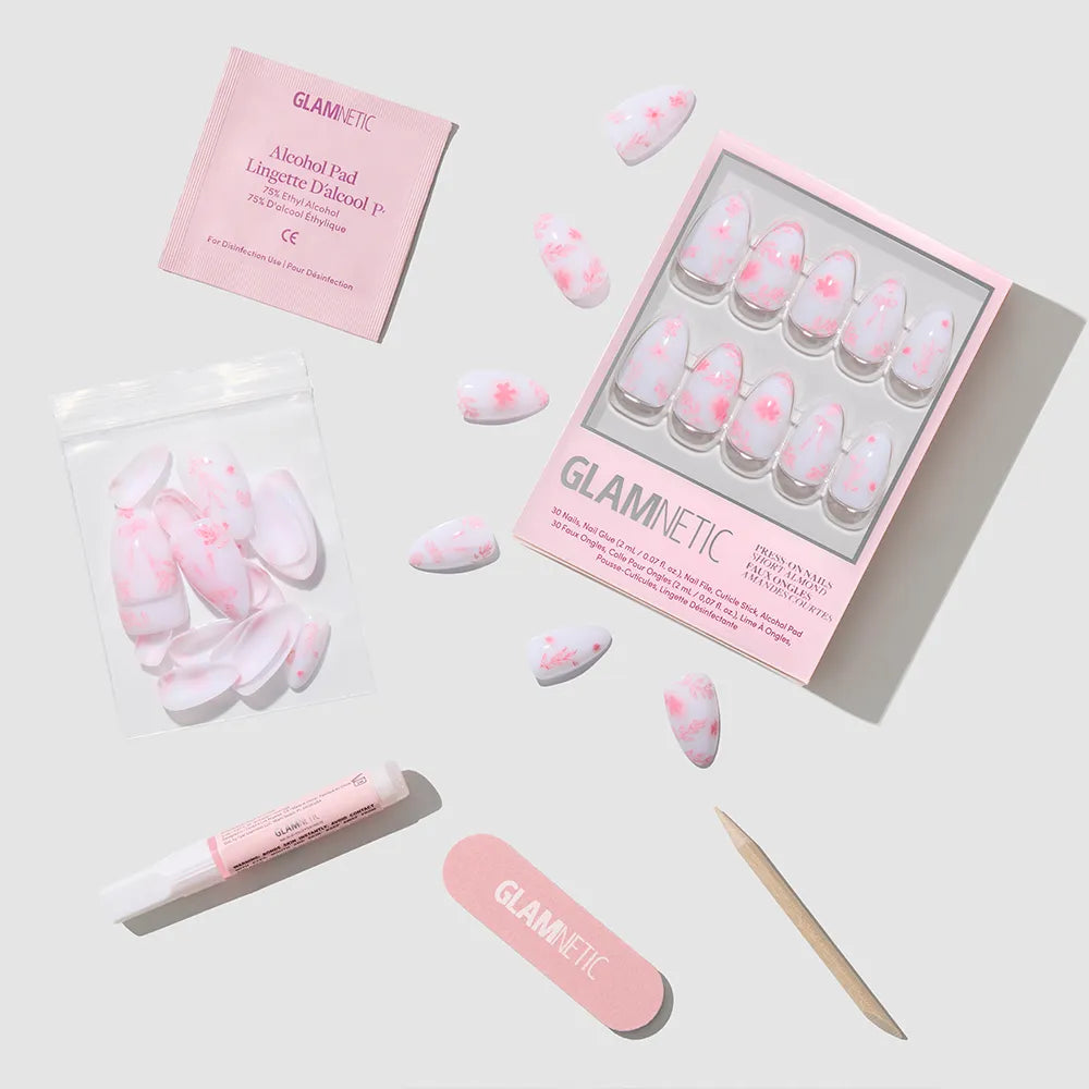 The glamnetic Fleur Amour set features short almond vegan, cruelty-free pink blossom nails, plus glue, alcohol pad, nail file, cuticle stick, and extra nails—displayed neatly on a light gray background. - Product image