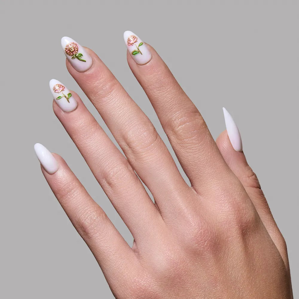 A hand with short almond white nails featuring 3D roses and green leaves from the glamnetic Floral Glow set, elegantly displayed against a plain gray background. - Product image