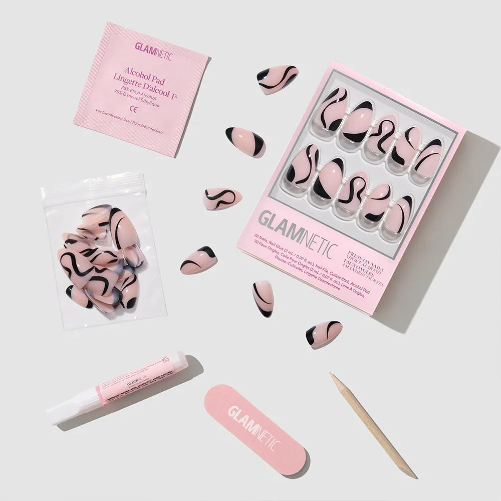 A flat lay of glamnetic’s Ink Wave press-on nail kit, featuring glossy pink and black swirl nails, nail glue, alcohol pad, nail file, wooden cuticle stick, and extra nails in a small bag. - Product image