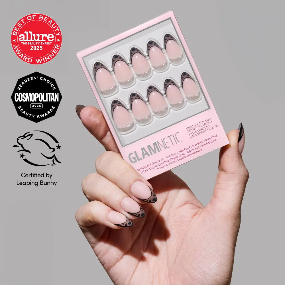 A hand with short almond nails, pink base, and black swirl French tip (Love Noir by glamnetic) holds a glamnetic press-on nails package. Allure and Cosmopolitan award badges and the Leaping Bunny cruelty-free logo are visible.